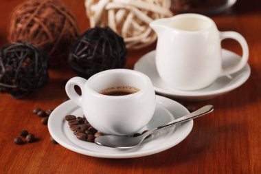 Beyaz espresso kahve fincanı, kavrulmuş kahve çekirdekleri ve süt sürahi ahşap masa arka plan üzerinde. Kahve molaları ve hizmet kahve kavramı