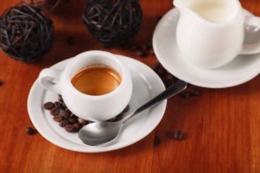 Beyaz espresso kahve fincanı, kavrulmuş kahve çekirdekleri ve süt sürahi ahşap masa arka plan üzerinde. Kahve molaları ve hizmet kahve kavramı