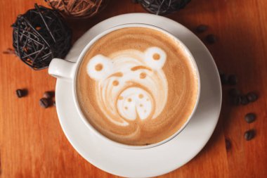 Fincan cappuccino kahve ahşap arka plan üzerinde ayı yakın çekim şeklinde bir latte sanat desenli beyaz. Bir kafede kahve yapma kavramı