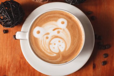 Fincan cappuccino kahve ahşap arka plan üzerinde ayı yakın çekim şeklinde bir latte sanat desenli beyaz. Bir kafede kahve yapma kavramı