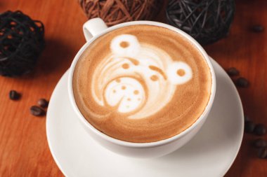Fincan cappuccino kahve ahşap arka plan üzerinde ayı yakın çekim şeklinde bir latte sanat desenli beyaz. Bir kafede kahve yapma kavramı