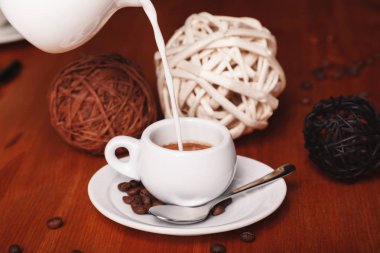 Süt sütçü küçük bir fincan espresso kahve ahşap arka plan üzerinde içine dökme. Kahve molaları ve hizmet kahve kavramı