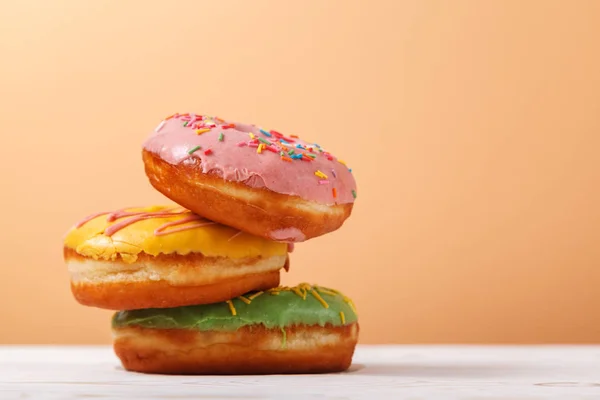 Bej renkli arka plan üzerinde üç adet çok renkli donut. Uzay kopyalayın. Tatlılar fırına beslenme kavramı. Hanuka