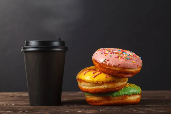 Färgglada munkar och kaffe i en svart papper kopp på en svart bakgrund. Bageri-menyn designkoncept. Hanukkah bakgrund. — Stockfoto