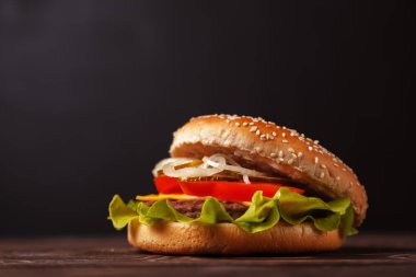Burger peynir, pastırma, marul, soğan ve domates yakın çekim karanlık bir arka plan ile. Fast food, abur cubur kavramı