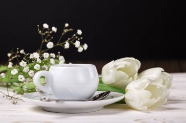 Bir fincan kahve ve beyaz laleler koyu arka plan üzerinde. Anneler gününde kahvaltı kahve servisi kavramı. Cafe menü
