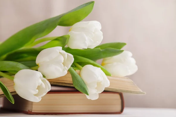 Beautiful composition with white tulips and old books on a beige blurred background in the morning light. Spring reading