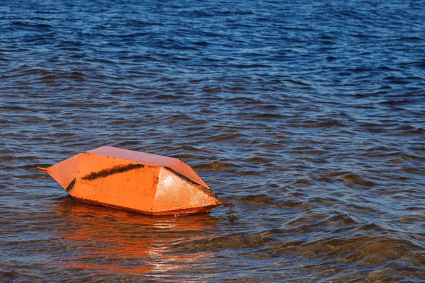 Safety on the water. A large orange buoy horizontally lies near the shore on the water of the Bay of the river.