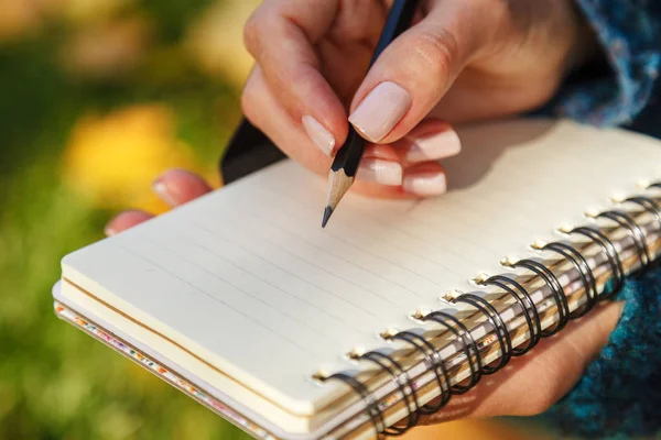 女性の手は柔らかい日差しの中で黄色の葉に対して紙のノートと鉛筆を保持します。秋の気分、コピースペース — ストック写真
