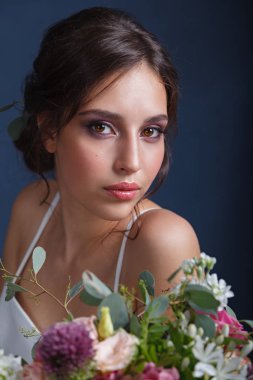 Çiçek bir buket ile beyaz bir elbise profesyonel makyaj ve saç modeli ile büyüleyici bir genç gelin portresi