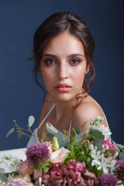 花の花束と白いドレスでプロのメイクアップと髪型と魅力的な若い花嫁の肖像画 ストック写真