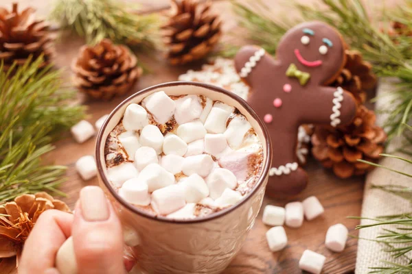 Hombre de jengibre y chocolate caliente con malvaviscos, en el fondo de las ramas del árbol de Navidad en una mesa de madera — Foto de Stock