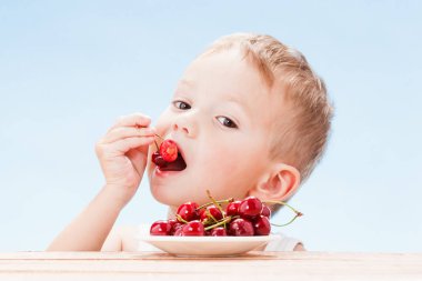 Kırmızı meyveler ile çocuk, çocuk yiyor ve kiraz seçer. Mavi gökyüzü arka plan.