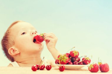 Küçük sevimli beyaz çocuk kiraz daireler ile gökyüzü arka plan üzerinde masada yemek