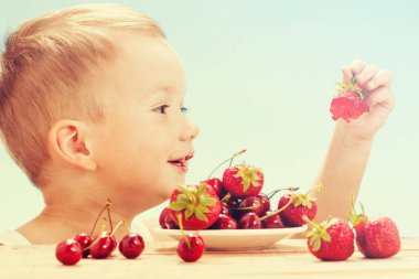 Küçük sevimli beyaz çocuk kiraz daireler ile gökyüzü arka plan üzerinde masada yemek