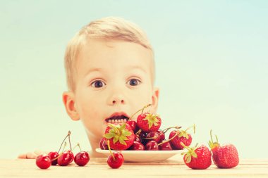 Küçük sevimli beyaz çocuk kiraz daireler ile gökyüzü arka plan üzerinde masada yemek