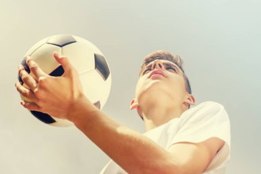 Mavi gökyüzü arka plan üzerinde bir futbol topu ile genç çocuk