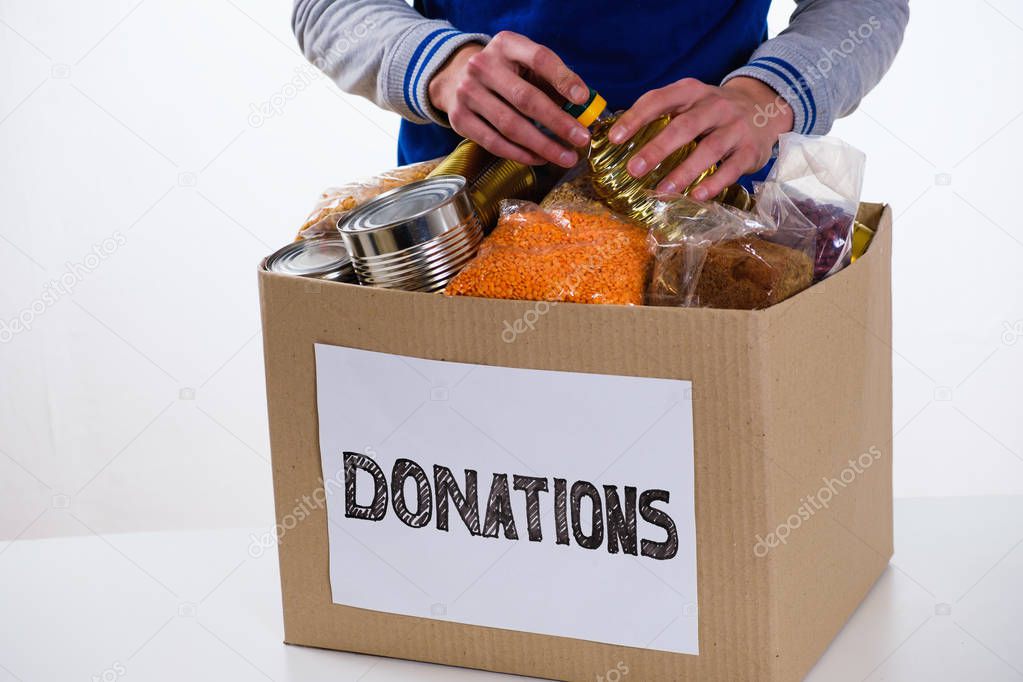 Food in a donation cardboard box, isolated on white background, volunteer fills the box.