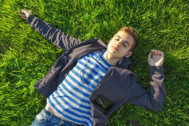 Genç çocuk smartphone ve müzik dinler ile yeşil çayır üzerinde yalan