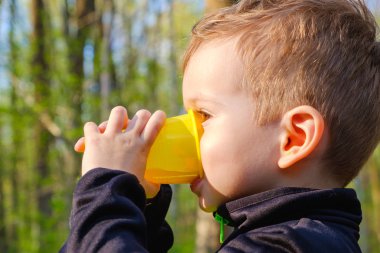 Doğada uzun bir yürüyüş içinde küçük bir çocuk içecekler bir plastik cam.