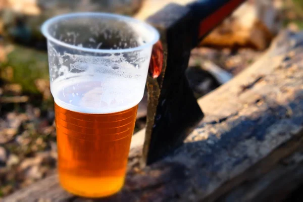 The axe on the stump with beer in a plastic cup