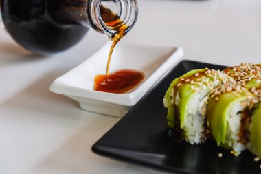 Lezzetli soya soslu kase. Yılan balığı ve avokadoyla suşi rulosu. Geleneksel Japon yemekleri.