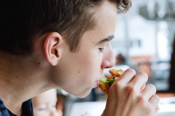 オフにかまれる テーブルの上の白いプレートにハンバーガーとフライド ポテトを食べる少年 — ストック写真