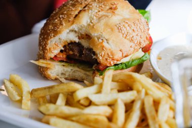 Hamburger ve patates kızartması masada beyaz tabakta, ısırılıp koparılmış.