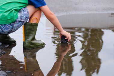 Çocuk bir yeşil Boots göletlerde atlama. Bir çocuk yağmur, parlak bir yağmurluk duruyor. Sonbahar park oynayan çocuk. Herhangi bir hava açık eğlence