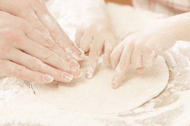 Anne ve çocuk elleri hamuru un, merdane ve buğday ile yukarıdan kırsal ahşap masa üzerinde hazırlar. Ekmek ya da pizza için ev yapımı pasta. Fırın arka planı.
