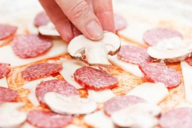Aşçı mozzarella ve salamın üzerine mantar koyup yakın plan çiğ pizza yapıyor.
