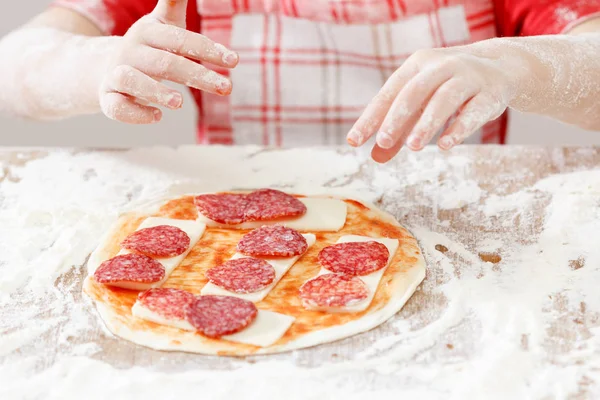 Cook putting salami over mozzarella and tomato on a raw pizza close-up