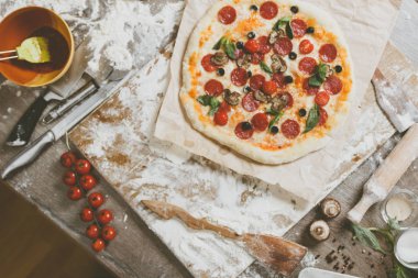 En tepedeki manzarada, malzeme, domates, salam, un, hamur fesleğeni, baharat, mozzarella ve ahşap masa üstünde mantarlı pizza pişiriliyor.