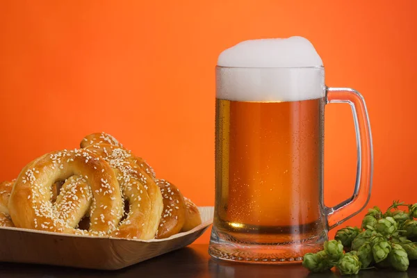 Pint of beer with ingredients for homemade beer on red background with pretzel