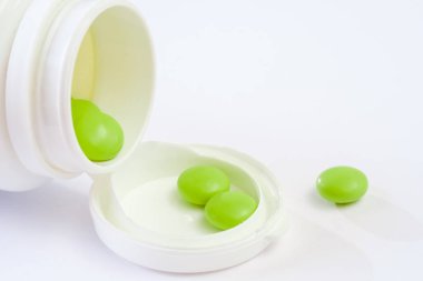 Plastik şişenin yanında bir sürü ilaç duruyor. Haplar ve şişeler beyazdır. Beyaz arkaplanda izole