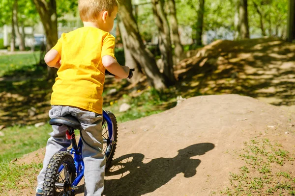 Маленький хлопчик їде зі своїм першим велосипедом у міському парку. Щаслива дитина в барвистому одязі. Дозвілля для дітей на відкритому повітрі . — стокове фото