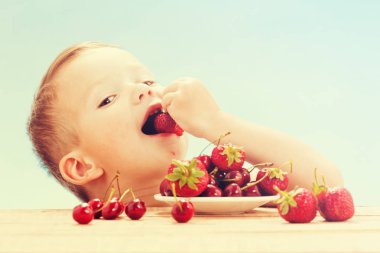 Küçük sevimli beyaz çocuk gökyüzünde masada tabaklar ile kiraz yeme