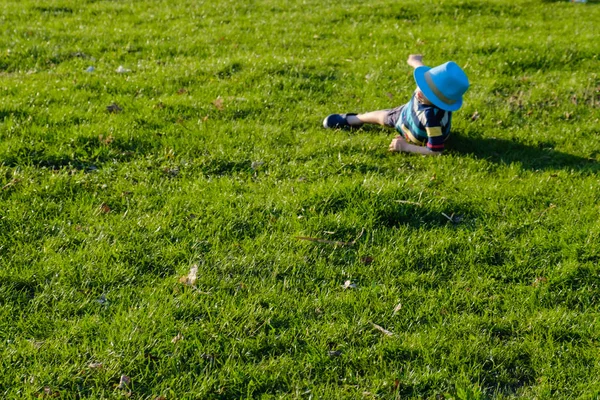 Un niño guapo tirado en la hierba. El pequeño soñador yace en el prado con sombrero. Niño en la naturaleza fuera de la ciudad. Vacaciones sin preocupaciones — Foto de Stock