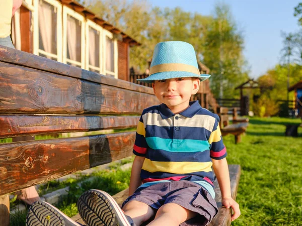 Niño sonriente sentado en un banco del parque con prado verde en el fondo — Foto de Stock