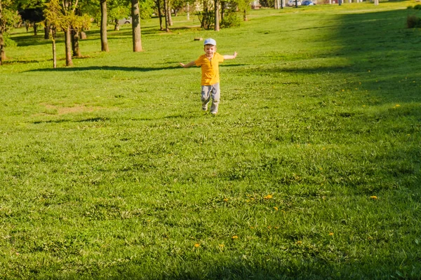 Lindo chico corriendo a través de hierba und sonriendo . —  Fotos de Stock