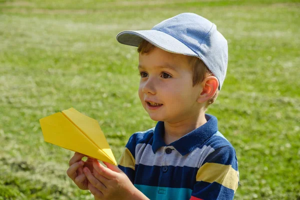 Menino brincando com um avião de brinquedo amarelo no parque em um dia ensolarado — Fotografia de Stock