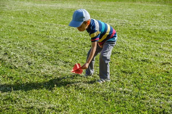 Chico jugando con un avión rojo de juguete en el parque en un día soleado — Foto de Stock