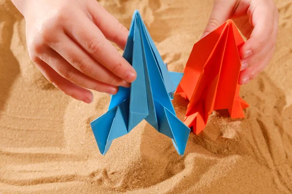 Niño feliz jugando con papel de origami hecho a mano, cohete en arena de playa, concepto de puesta en marcha —  Fotos de Stock