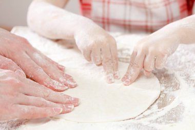 Anne ve çocuk elleri hamuru un, merdane ve buğday ile yukarıdan kırsal ahşap masa üzerinde hazırlar. Ekmek ya da pizza için ev yapımı pasta. Fırın arka planı.