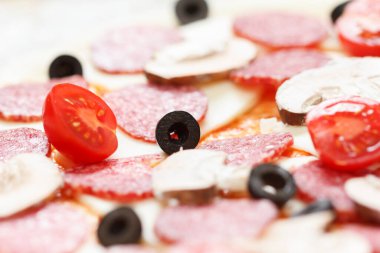 Mozzarella, domates ve salam üzerine zeytinli çiğ pizza hamuru.