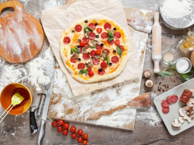 En tepedeki manzarada, malzeme, domates, salam, un, hamur fesleğeni, baharat, mozzarella ve ahşap masa üstünde mantarlı pizza pişiriliyor.