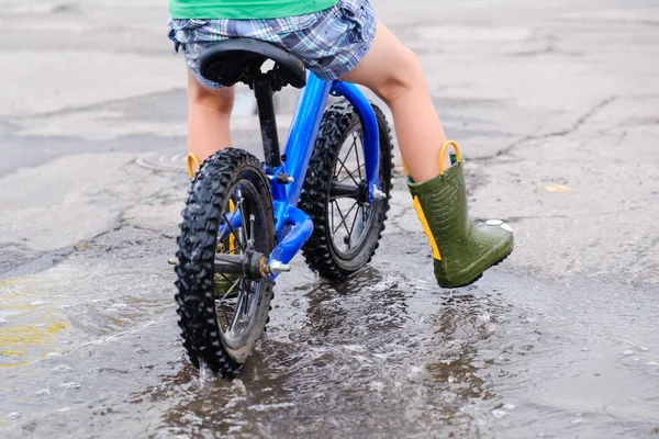 child on a balance bicycle at asphalt road in summer. Bike in the park moving through puddle on rainy day