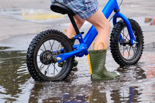 child on a balance bicycle at asphalt road in summer. Bike in the park moving through puddle on rainy day