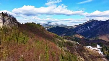 Ormanla çevrili kayalık bir tepeyi, manzarası olan hava hızıyla yakalıyor. Sahnede, Nisan ayındaki bahar mevsimini temsil eden kabarık bulutlu mavi gökyüzü yer alıyor.