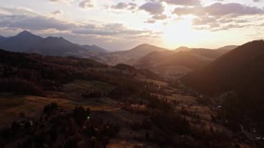 Karpat kırsalının hava manzarası, alacakaranlıkta gün batımının altın ışığıyla aydınlatılan çayır ve ormanları gösteriyor, barışçıl ve sakin bir atmosfer yaratıyor..